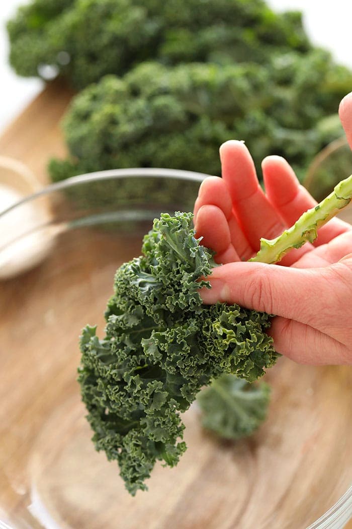 A hand removing a stem from a piece of kale