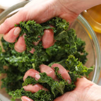 A person's hands expertly massage fresh kale in a bowl.