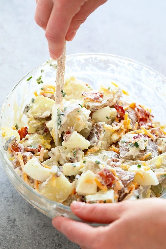 A hand mixing loaded baked potato salad