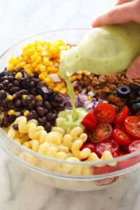 pouring dressing on top of pasta salad.