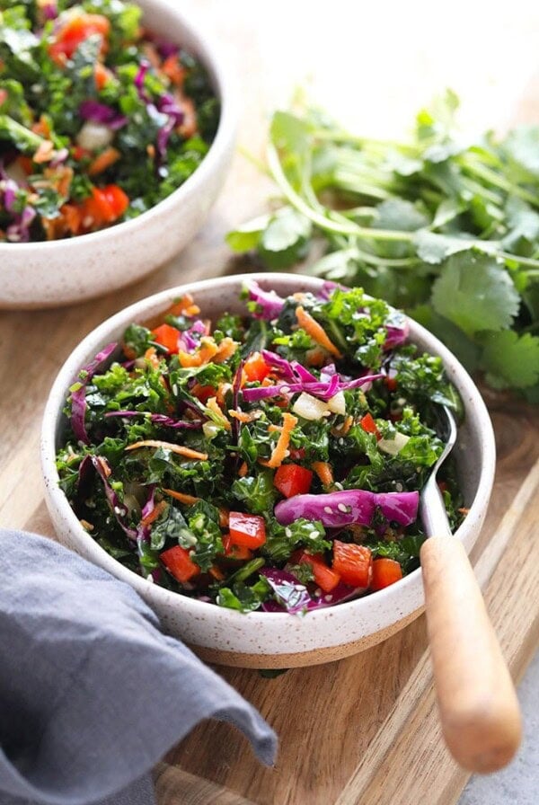 Two bowls of Asian kale salad on a cutting board.