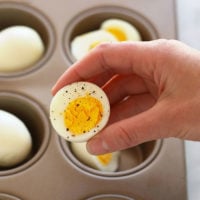 A person using an oven to hard boil eggs in a muffin tin.