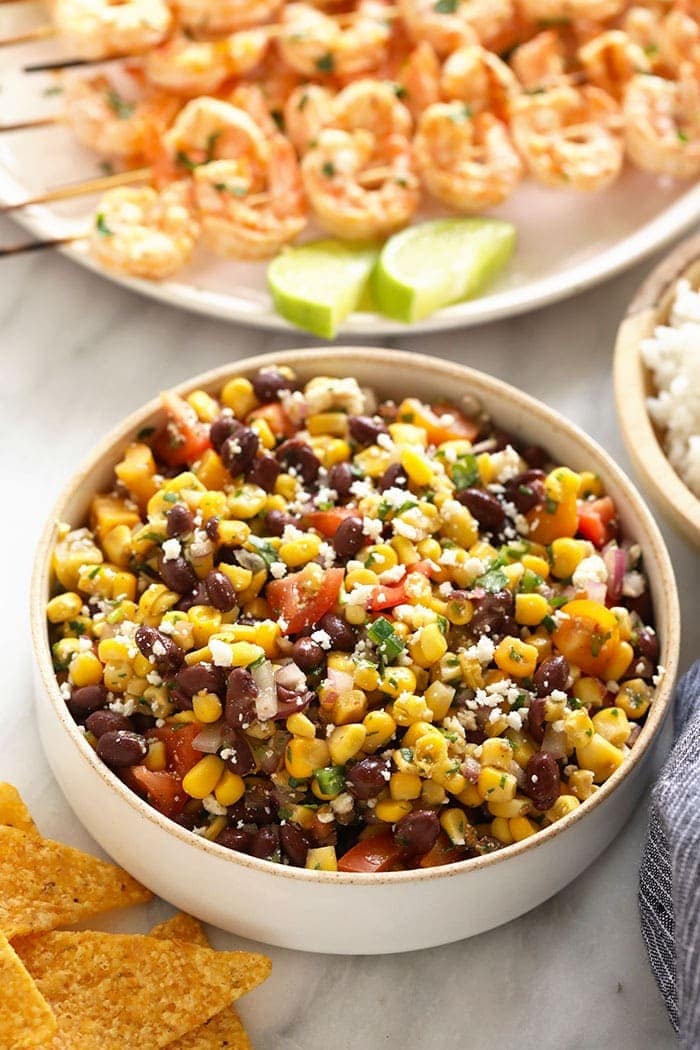 black bean corn salad with grilled shrimp on skewers in the background