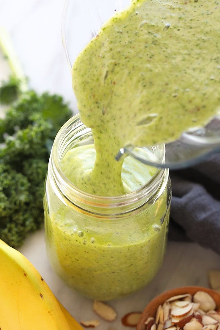 kale smoothie being poured from a blender to a mason jar.