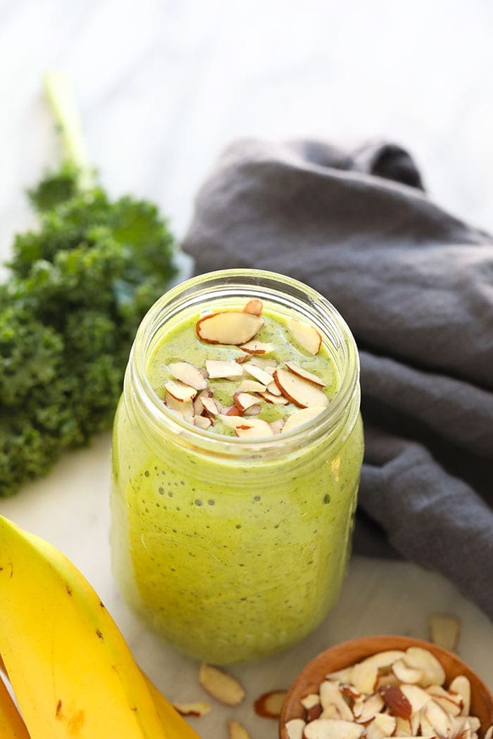 Get your daily greens here! This is the most delicious kale smoothie you'll ever make! It's packed with nutrient dense kale, frozen bananas and the perfect flavor punch of orange juice and fresh ginger. Whip up this green smoothie in 5 minutes and you're off and running with a healthy breakfast or snack on the go. kale smoothie in a mason jar.