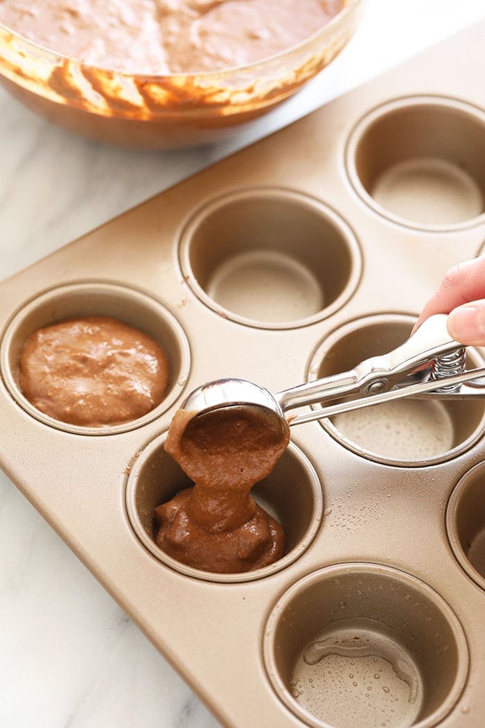 Scooping healthy chocolate muffin batter into a muffin tin