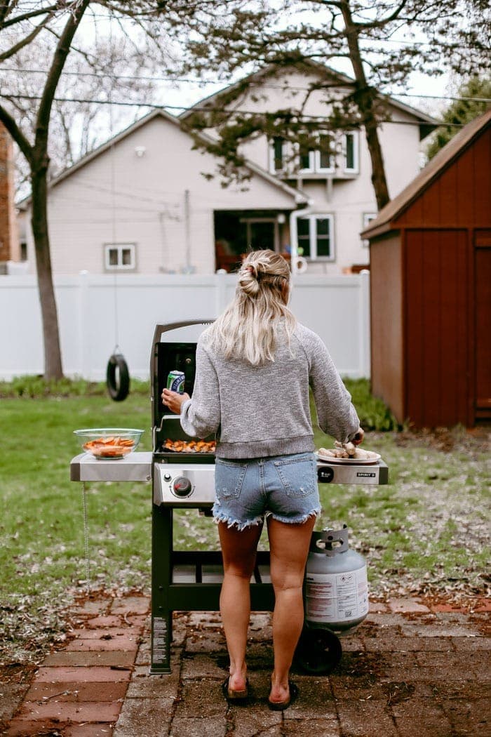 Ever heard of beer brats? Beer boiled brats are by far the most delicious way to cook brats. Start by boiling your brats in beer and then finish them off with a sear on the grill, some ketchup & mustard, and relish too! girl grilling with beer