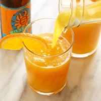 a glass of orange juice is being poured into a beermosa.