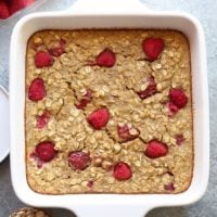 A white baking dish with raspberries, oats, and banana oatmeal toppings.