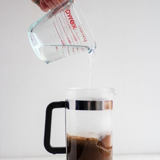 A person using a French press to pour coffee into a glass mug.