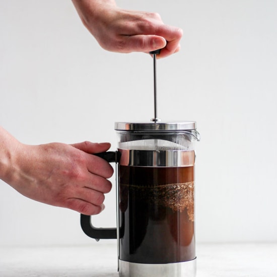 A person using a French press to pour coffee.