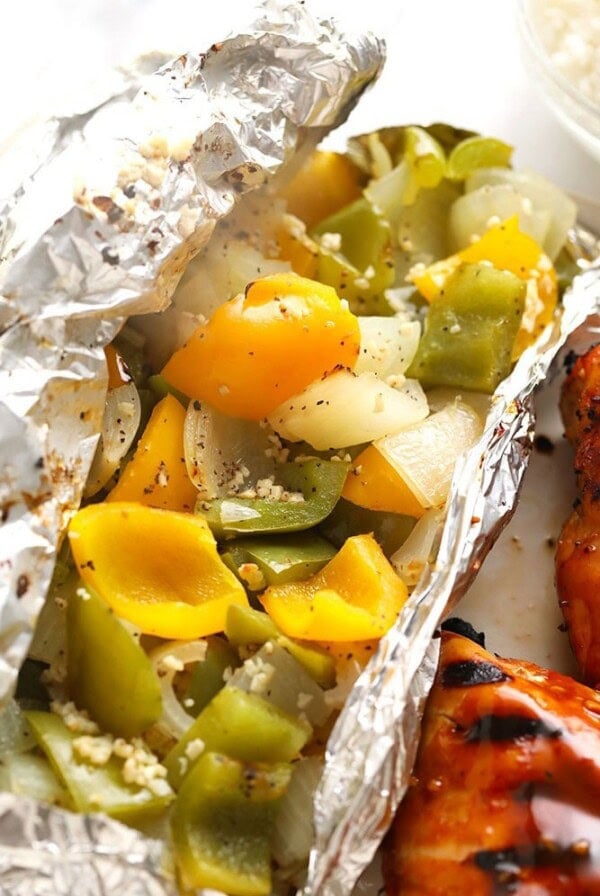 A foil-wrapped plate with grilled chicken, peppers, and rice.