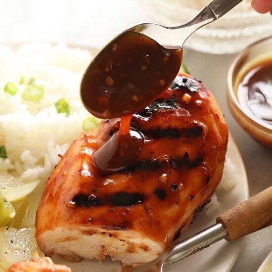 A person is marinating chicken in a homemade teriyaki sauce on a plate.