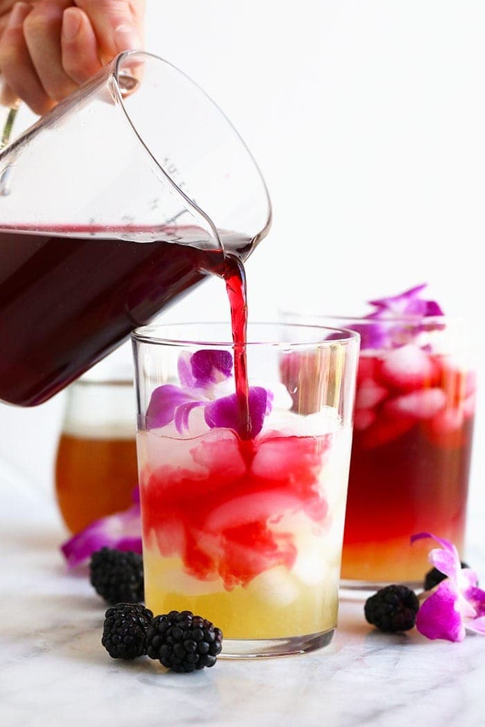 hibiscus arnold palmer drink in a glass topped with edible flowers