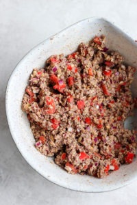 a white bowl with a black bean burger and peppers.