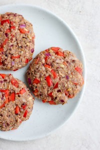 three black bean burgers topped with red peppers and onions on a plate.