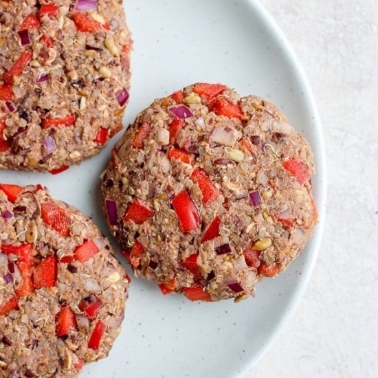 three black bean burgers topped with red peppers and onions on a plate.