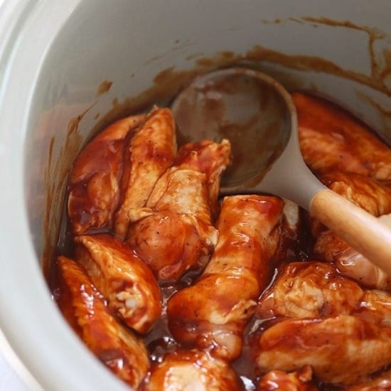bbq chicken in a crock pot with a wooden spoon.