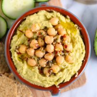 a bowl of avocado hummus with chickpeas and cucumbers.