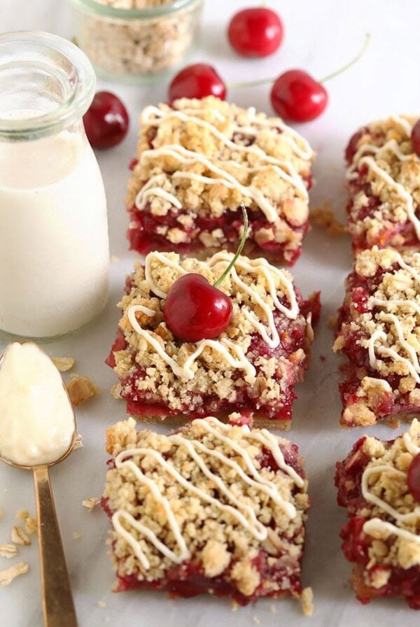 Cherry oatmeal bars resembling cherry cobbler on a marble countertop with a glass of milk.