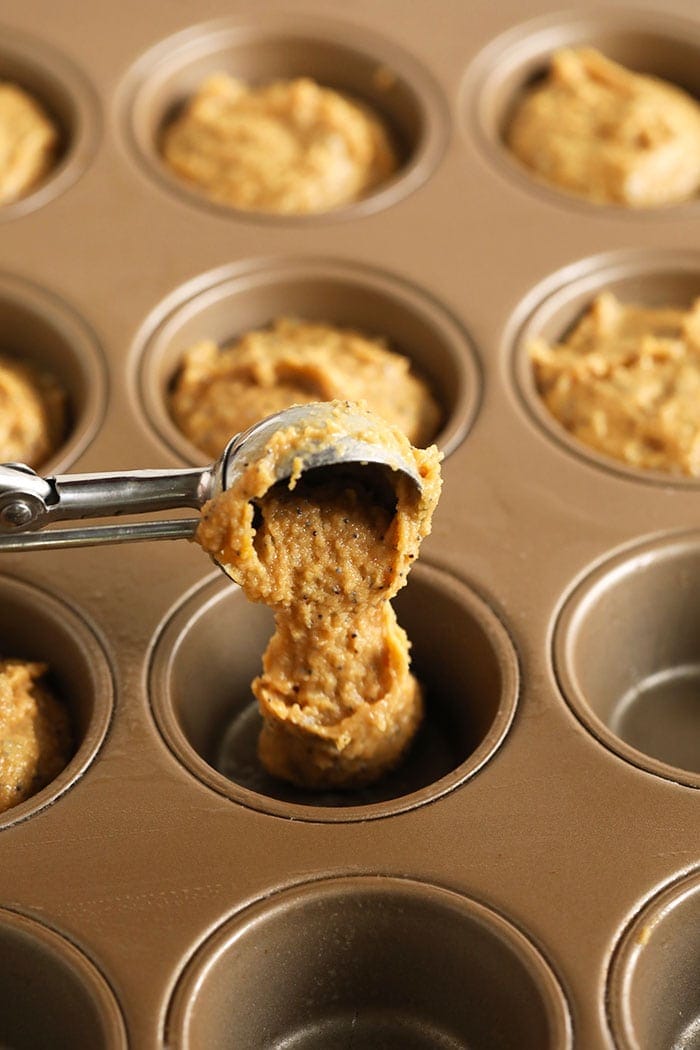 scooping lemon poppy seed muffin batter into a muffin tin