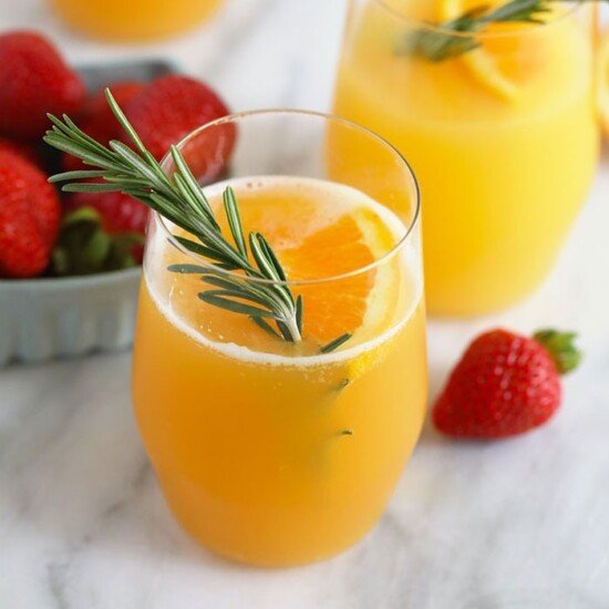Two glasses of beermosa with strawberries and sprigs of rosemary.