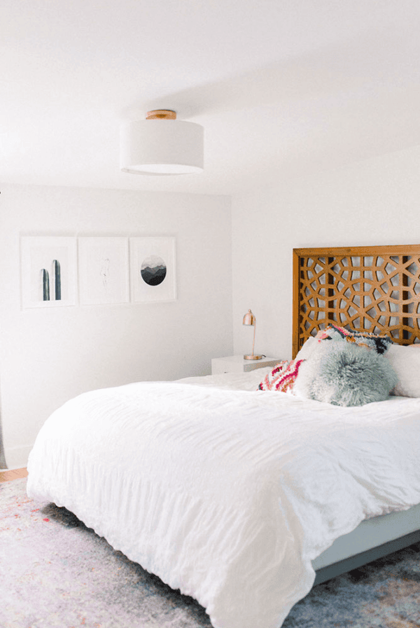 A bedroom with a white bed and colorful rug is illumined by Velux skylights.