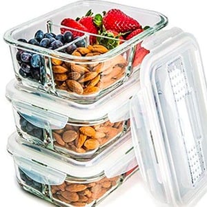 a stack of glass meal prep containers filled with nuts and berries.