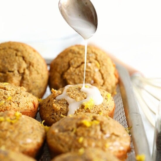 A spoon is drizzling over a tray of lemon poppy seed muffins.
