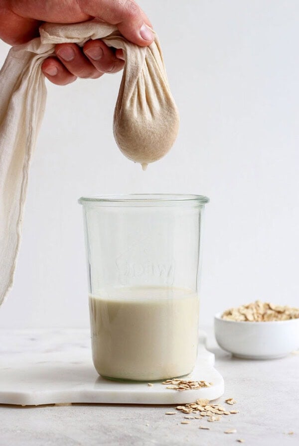 A person prepares a oat milk recipe by pouring oats into a glass of milk.