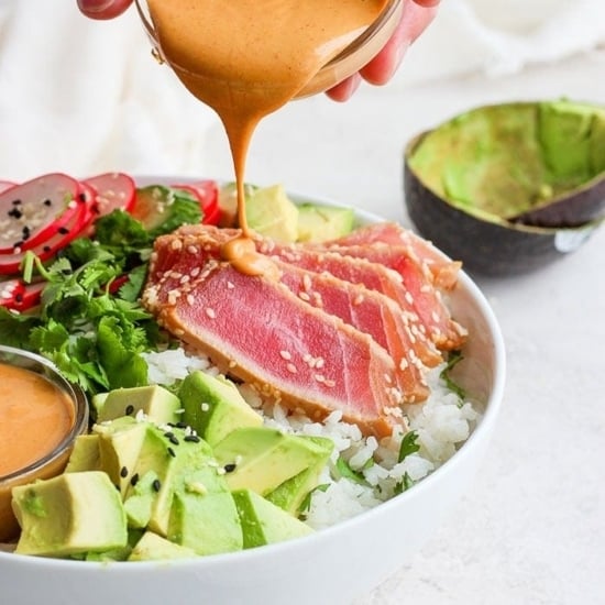 a person drizzling a creamy tahini sauce on a nutritious ahi poke bowl.