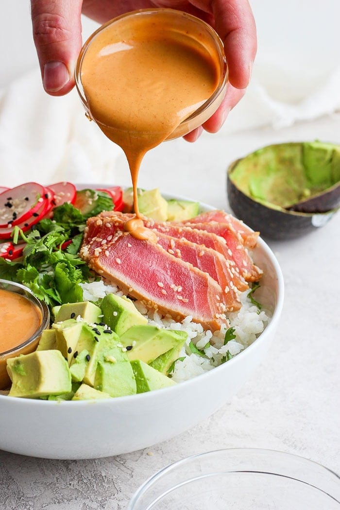 Drizzling almond dressing onto the poke bowl