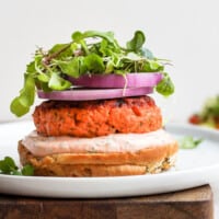 Delicious salmon burgers served with arugula and red onion on a white plate.