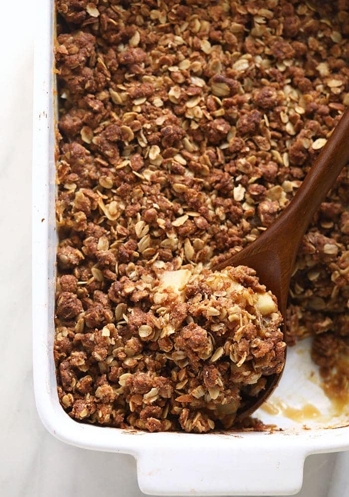 A white baking dish with a spoonful of granola in an apple crisp recipe.