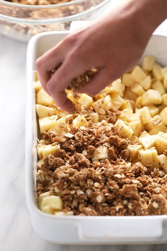 This delicious apple crisp recipe is made with a simple apple filling and a delicious crumble topping. Make this healthier, fall-inspired dessert today! sprinkling crumble topping on apples