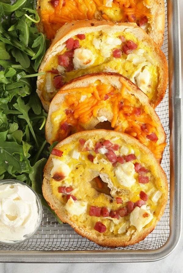 a tray of bagels topped with bacon, arugula, and ham.