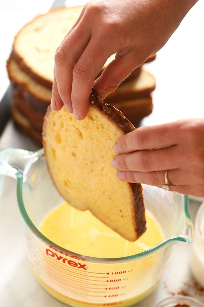 whole wheat bread being dipped in egg mixture for sheet pan french toast