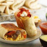 Fajita breakfast burritos on a plate with guacamole and salsa.