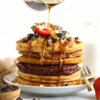 A stack of healthy pancakes with syrup being poured over them.