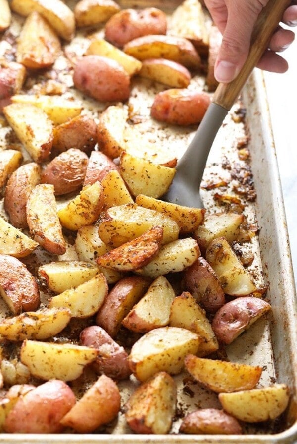 A person scooping roasted red potatoes from a baking sheet.