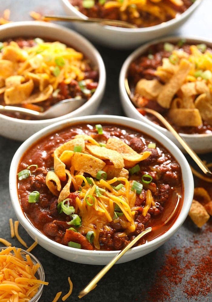 Four bowls of the best chili topped with cheese and served with tortilla chips.