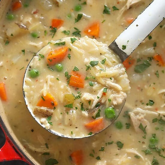 A creamy s،ful of chicken noodle soup with carrots and peas.