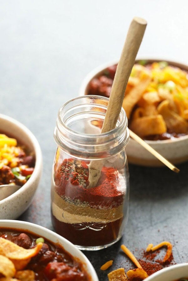 Homemade chili seasoning in a jar, accompanied by a wooden spoon.