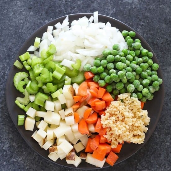 Chopped vegetables on a black plate accompany creamy chicken noodle soup.
