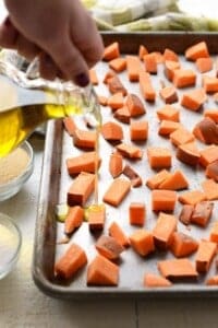 Drizzling olive oil onto sweet potato cubes on a baking sheet.