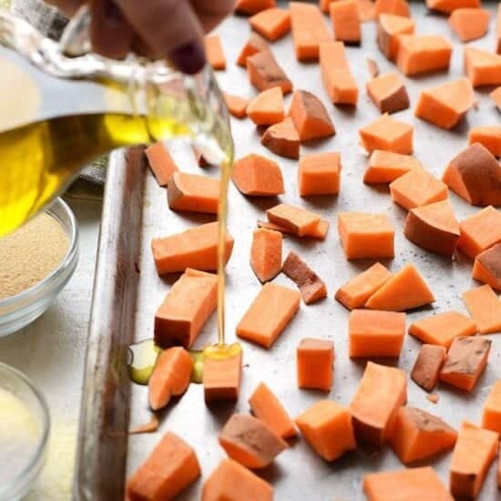 Drizzling olive oil onto sweet potato cubes on a baking sheet.