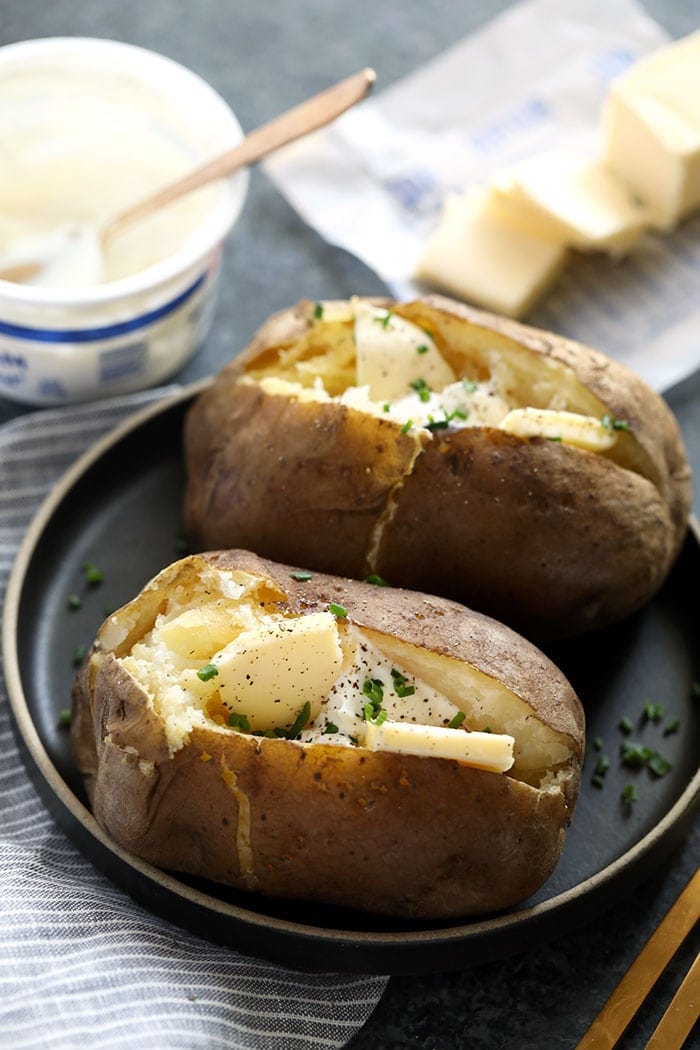 Olla de barro papas al horno cubiertas con mantequilla en un plato