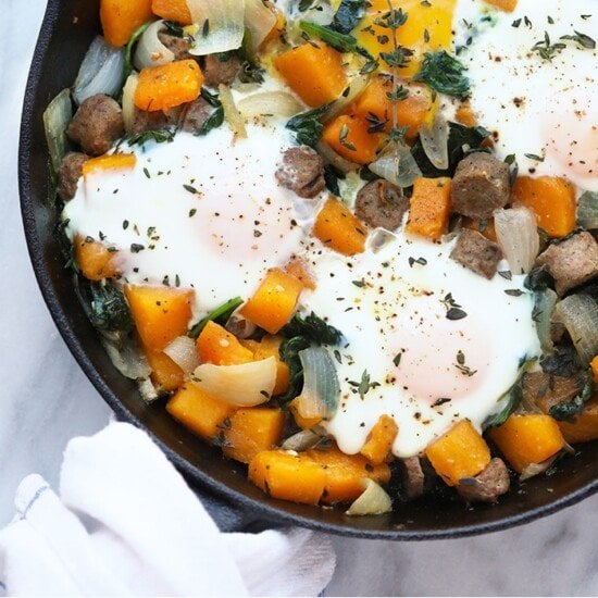 A skillet filled with eggs, butternut squash, greens, and a breakfast hash.