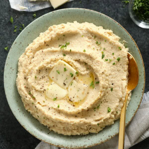 Cauliflower mashed potatoes topped with hummus, served on a plate with a spoon.