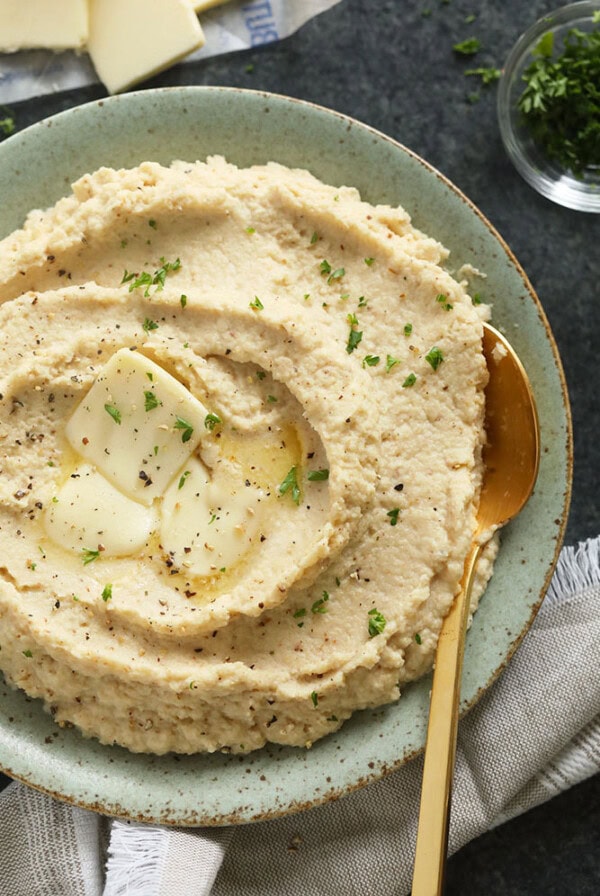 Hummus served on a plate with a spoon and garnished with parsley.